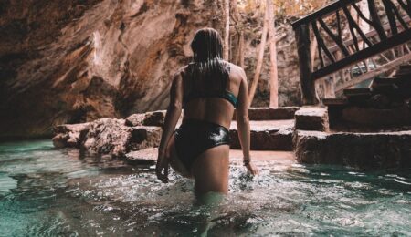woman in bikini walking out of water inside cave